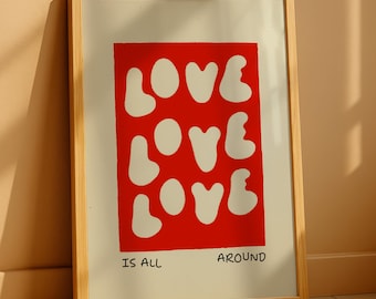 May include: Framed art print with a red rectangle featuring the word "LOVE" repeated three times in white, with "IS ALL AROUND" below. The frame is light wood, and the background is a neutral color.