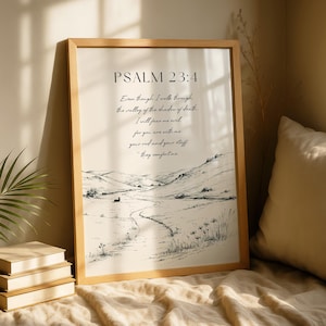 May include: A framed print featuring the text "PSALM 23:4" and a quote about overcoming fear. The artwork depicts a black and white landscape with a path through hills. The frame is light brown. The print is displayed indoors.