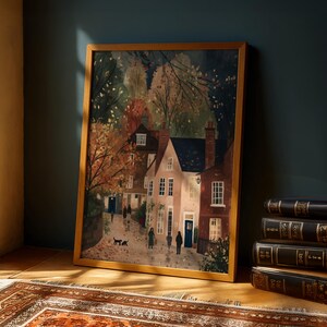 K&ouml;nnte beinhalten: Ein gerahmter Kunstdruck, der eine malerische Dorfszene mit Menschen zeigt, die auf einer Kopfsteinpflasterstra&szlig;e spazieren. Das Kunstwerk zeigt Geb&auml;ude mit wei&szlig;en und roten Backsteinfassaden, umgeben von B&auml;umen mit Herbstlaub. Der Rahmen ist hellbraun.