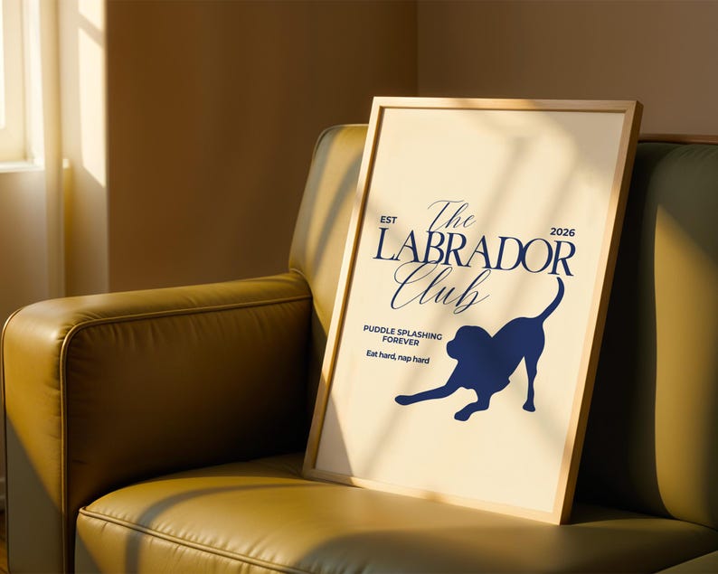 Puede incluir: Un p&oacute;ster enmarcado con fondo beige claro y marco de madera. El p&oacute;ster presenta el texto "The Labrador Club" en azul marino, junto con una silueta de un perro Labrador. Tambi&eacute;n se incluye el texto "Puddle splashing forever" y "Eat hard, nap hard".