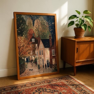 K&ouml;nnte beinhalten: Ein gerahmter Kunstdruck zeigt eine malerische Dorflandschaft mit Geb&auml;uden, B&auml;umen und Figuren. Das Kunstwerk weist eine warme Farbpalette aus Braun-, Orange- und Blaut&ouml;nen auf und hat einen Holzrahmen. Der Druck wird neben einem Holzschrank und einer Topfpflanze pr&auml;sentiert.