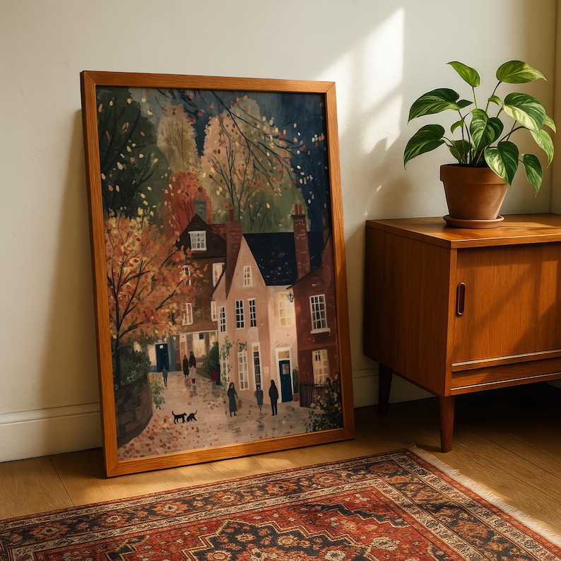 K&ouml;nnte beinhalten: Ein gerahmter Kunstdruck zeigt eine malerische Dorflandschaft mit Geb&auml;uden, B&auml;umen und Figuren. Das Kunstwerk weist eine warme Farbpalette aus Braun-, Orange- und Blaut&ouml;nen auf und hat einen Holzrahmen. Der Druck wird neben einem Holzschrank und einer Topfpflanze pr&auml;sentiert.
