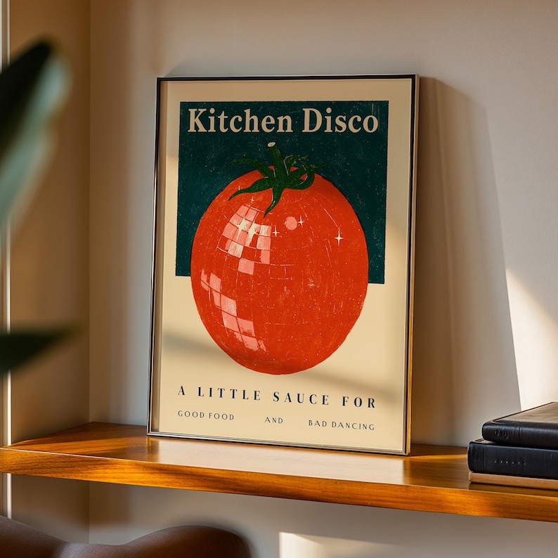 a framed poster with a large tomato graphic and text, placed on a wooden shelf against a white wall.