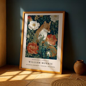 A framed print of William Morris' botanical ornament, featuring a fox surrounded by flowers, is displayed on a wooden floor against a blue wall.