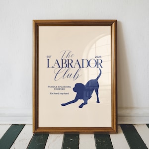 Puede incluir: Una impresi&oacute;n enmarcada con un marco de madera color oro. La impresi&oacute;n presenta una silueta azul marino de un Labrador Retriever y las palabras "The Labrador Club" en una fuente decorativa. El texto adicional dice "Puddle splashing forever" y "Eat hard, nap hard."
