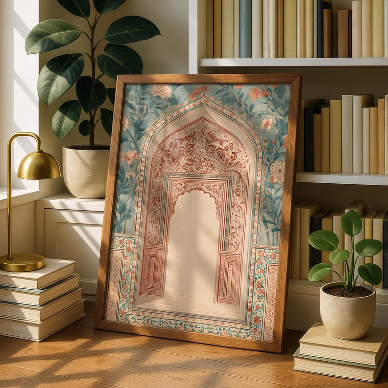 May include: A framed print featuring an ornate archway design with floral and geometric patterns in shades of red, pink, and teal. The artwork is set in a wooden frame and leans against a wall near a bookshelf and plants.
