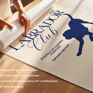 Puede incluir: Un p&oacute;ster enrollado con una silueta de Labrador azul marino y las palabras "LABRADOR Club" y "PUDDLE SPLASHING FOREVER". El p&oacute;ster est&aacute; sobre un fondo beige claro. Tambi&eacute;n se incluye el texto "Eat hard, nap hard".
