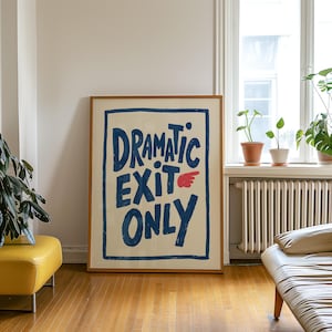 May include: A rectangular framed wall art piece featuring a cream-coloured background with a thick blue border. The text reads "DRAMATIC EXIT ONLY" in bold, hand-drawn blue lettering, accompanied by a small, stylised red wing icon next to the word "EXIT."