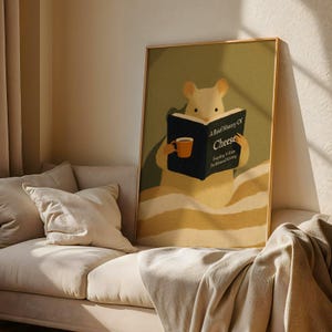 May include: A framed art print shows a cartoon mouse reading a book titled "A Brief History Of Cheese." The mouse holds a mug of coffee. The artwork has a warm colour palette with a gold frame, and is displayed on a beige sofa.