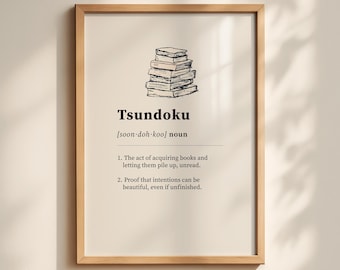 May include: A framed print with the word "Tsundoku" and its pronunciation. The print features a stack of books and the definition of Tsundoku: acquiring books and letting them pile up unread. The frame is a light brown color.
