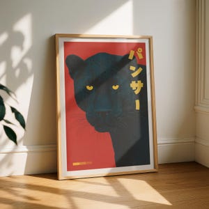 May include: Framed art print featuring a black panther against a red background. The panther's yellow eyes and the Japanese text "パンサー" are prominent. The artwork is in a wooden frame, leaning against a white wall.