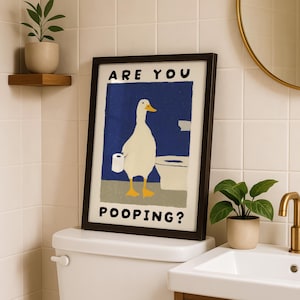 May include: Framed art print featuring a cartoon duck holding toilet paper, with the text "ARE YOU POOPING?" against a blue background. The artwork is in a black frame, placed above a toilet in a bathroom setting.