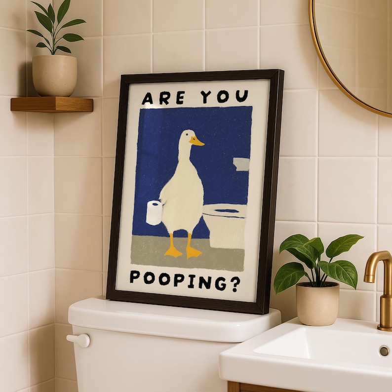 May include: Framed art print featuring a cartoon duck holding toilet paper, with the text "ARE YOU POOPING?" against a blue background. The artwork is in a black frame, placed above a toilet in a bathroom setting.
