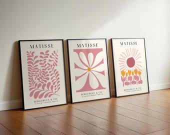 May include: Three framed art prints featuring Matisse designs in black frames. The left print shows pink leaves, the center shows a pink flower, and the right shows a pink sun over yellow flowers. Each print includes the text MATISSE BERGGRUEN & CIE.