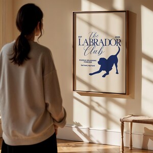 Puede incluir: Un p&oacute;ster enmarcado con fondo crema y texto y gr&aacute;ficos en azul oscuro. El texto dice "The Labrador Club" con una silueta de un perro labrador. El texto adicional incluye "Puddle splashing forever" y "Eat hard, nap hard."