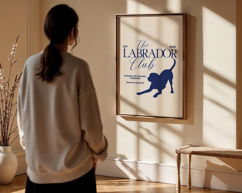 Puede incluir: Un p&oacute;ster enmarcado con fondo crema y texto y gr&aacute;ficos en azul oscuro. El texto dice "The Labrador Club" con una silueta de un perro labrador. El texto adicional incluye "Puddle splashing forever" y "Eat hard, nap hard."