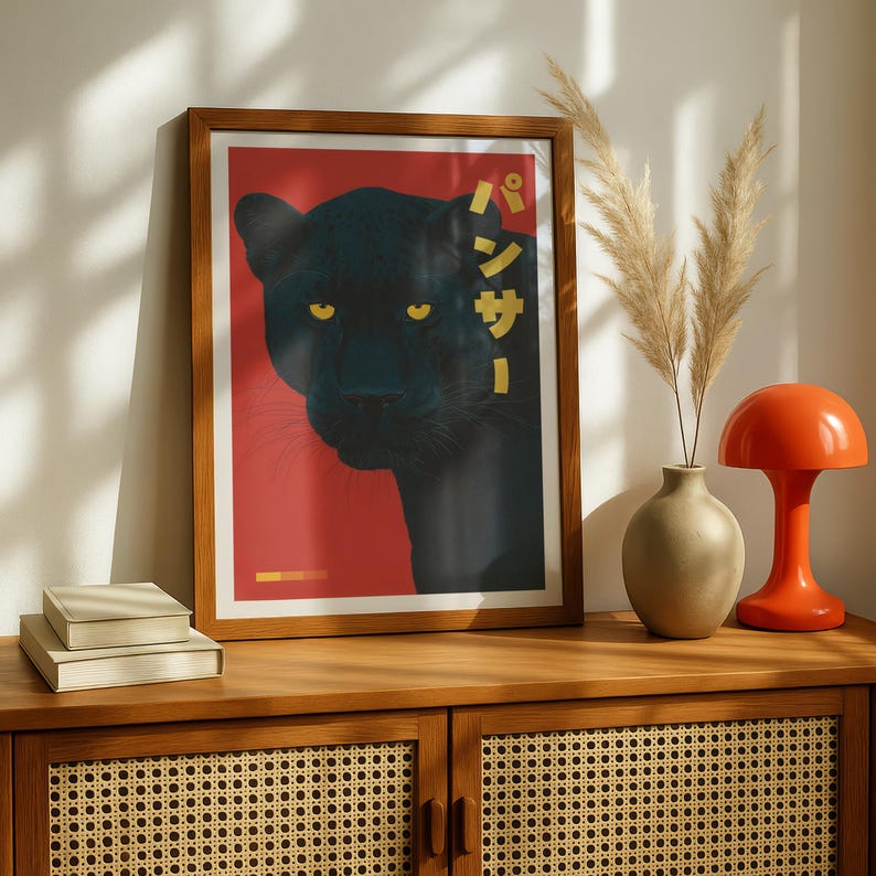 May include: Framed art print featuring a black panther on a red background. The panther's yellow eyes stand out against its dark fur. Japanese text is displayed vertically on the right side. The print is in a wooden frame.