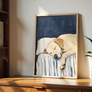 K&ouml;nnte beinhalten: Ein Gem&auml;lde eines Golden Retriever Hundes, der auf einem blau-wei&szlig; gestreiften Bett schl&auml;ft. Der Hund liegt zusammengerollt mit dem Kopf auf dem Kissen. Das Gem&auml;lde ist in einem hellen Holzrahmen gerahmt.