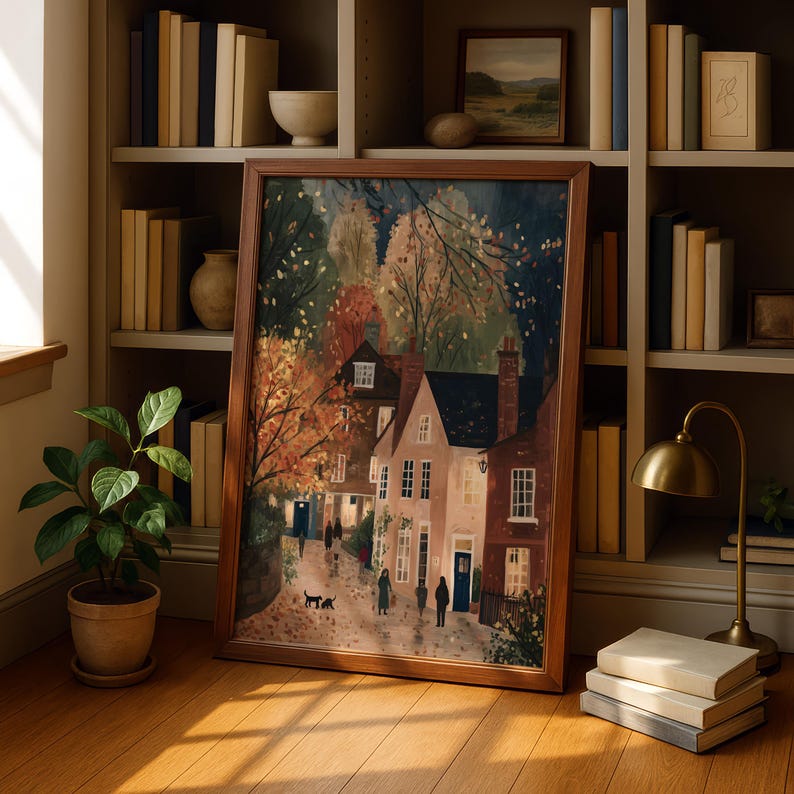 K&ouml;nnte beinhalten: Ein gerahmter Kunstdruck, der eine malerische Dorflandschaft mit H&auml;usern, B&auml;umen und Figuren zeigt. Das Kunstwerk hat warme Farben und einen braunen Holzrahmen. Der Druck wird auf einem Holzboden neben einer Topfpflanze und einem B&uuml;cherregal mit B&uuml;chern ausgestellt.