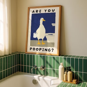 May include: A framed art print featuring a white duck holding toilet paper in a bathroom setting. The duck stands in front of a toilet against a blue background. The text "ARE YOU POOPING?" is displayed in black letters.