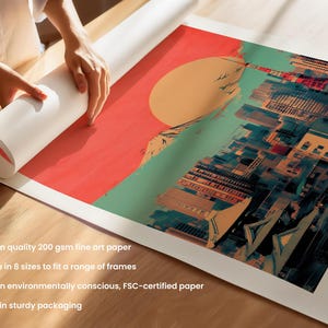May include: A colorful print of a cityscape with a large red sun in the background. The print is rolled up and being held by a person's hand. The print is printed on high-quality 200 gsm fine art paper and is available in 8 sizes to fit a range of frames. It is printed on environmentally conscious, FSC-certified paper and shipped in sturdy packaging.