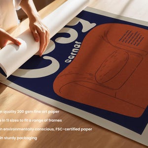 May include: An art print with a mid-century modern style illustration of an orange armchair on a navy blue background. The word "Corner" is in white, stylized text. The print is being unrolled. The paper is 200 gsm.