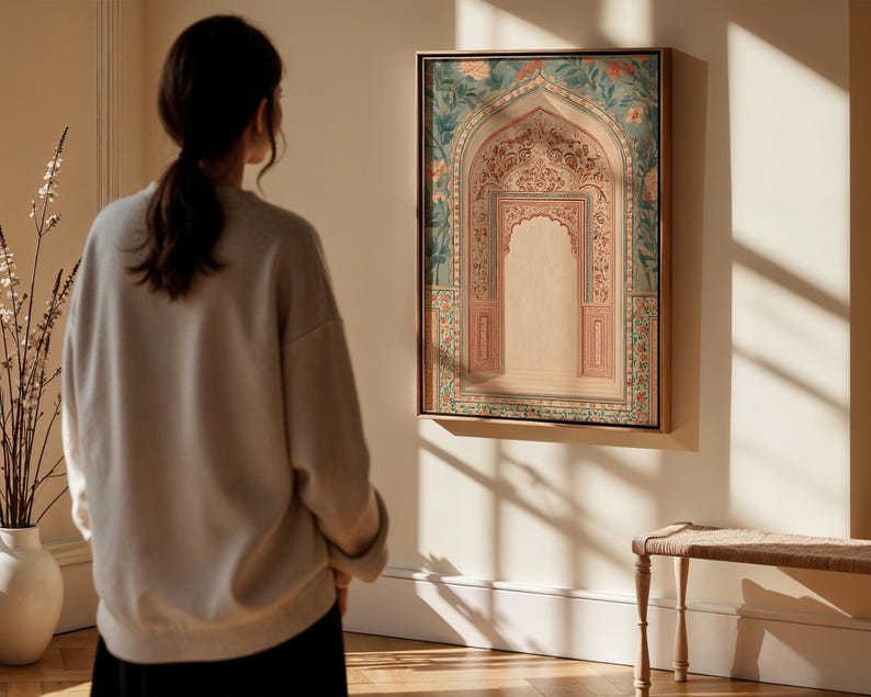 May include: A framed artwork depicting an ornate archway with floral and geometric patterns in shades of pink, green, and gold. The artwork is displayed on a white wall, and a person is standing in front of it, looking at the artwork.