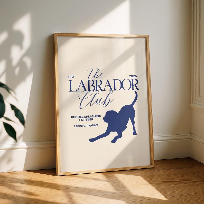 Puede incluir: Un p&oacute;ster enmarcado con fondo beige claro y marco de madera. El p&oacute;ster presenta el texto "The Labrador Club" en escritura azul marino, junto con una silueta de un perro Labrador. Tambi&eacute;n se incluye el texto "Puddle splashing forever" y "Eat hard, nap hard".