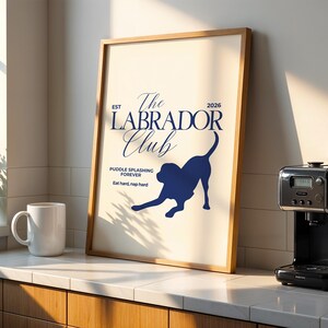 Puede incluir: Un p&oacute;ster enmarcado con el texto "The Labrador Club" y una silueta de perro. El p&oacute;ster est&aacute; en un marco de madera y se exhibe en una encimera junto a una taza blanca y una cafetera. Tambi&eacute;n se incluye el texto "Puddle splashing forever".