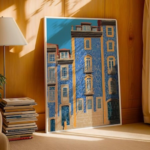K&ouml;nnte beinhalten: Ein gerahmter Kunstdruck, der eine detaillierte Illustration eines blauen Geb&auml;udes mit mehreren Fenstern, Balkonen und T&uuml;ren zeigt. Das Geb&auml;ude hat eine strukturierte Fassade und ist vor einem blauen Himmel platziert. Das Kunstwerk wird auf einem Holzboden neben einem Stapel B&uuml;cher ausgestellt.