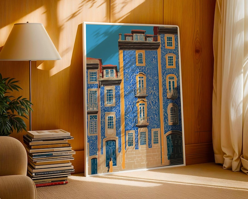 K&ouml;nnte beinhalten: Ein gerahmter Kunstdruck, der eine detaillierte Illustration eines blauen Geb&auml;udes mit mehreren Fenstern, Balkonen und T&uuml;ren zeigt. Das Geb&auml;ude hat eine strukturierte Fassade und ist vor einem blauen Himmel platziert. Das Kunstwerk wird auf einem Holzboden neben einem Stapel B&uuml;cher ausgestellt.