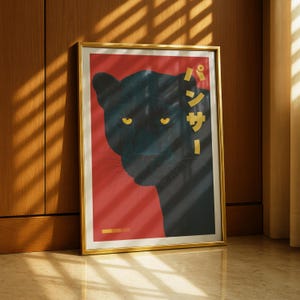 May include: Framed art print featuring a black panther illustration with yellow eyes against a red background. The print includes Japanese text in gold. The artwork is displayed in a gold frame and leans against a wooden wall.