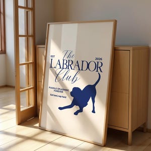 Puede incluir: Un p&oacute;ster enmarcado con fondo beige claro presenta el texto "The Labrador Club" en azul marino y la silueta de un Labrador. El p&oacute;ster incluye el texto "Puddle splashing forever" y "Eat hard, nap hard."