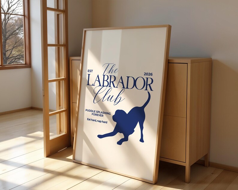 Puede incluir: Un p&oacute;ster enmarcado con fondo beige claro presenta el texto "The Labrador Club" en azul marino y la silueta de un Labrador. El p&oacute;ster incluye el texto "Puddle splashing forever" y "Eat hard, nap hard."