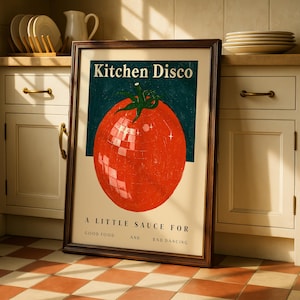 May include: A framed poster with the text "Kitchen Disco" above a red tomato illustration. The tomato has a disco ball effect. Below the tomato, the text reads "A Little Sauce For Good Food And Bad Dancing". The poster is in a kitchen setting.