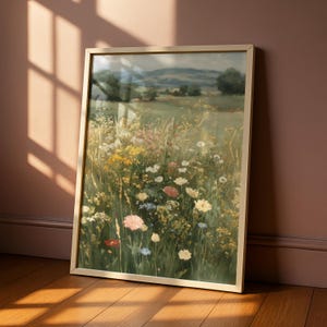 May include: A framed print depicting a wildflower meadow. The artwork shows a field of colourful flowers in shades of yellow, pink, white, and blue, with rolling hills in the background. The frame is a light gold colour.