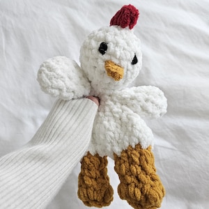 May include: White crocheted chicken plush toy with a red comb, black eyes, and a yellow beak. The chicken has brown crocheted legs.