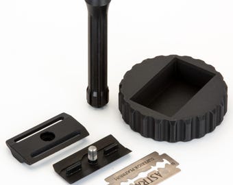 May include: A disassembled black safety razor set including a textured handle, a three-piece head assembly, and a single Astra Superior Platinum double-edge razor blade. The components are arranged on a plain surface for assembly.