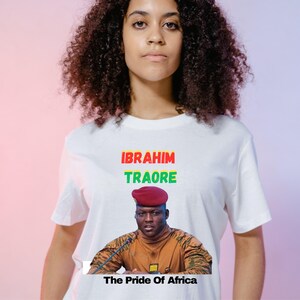 May include: White t-shirt featuring the text "IBRAHIM TRAORE" in red and green, with a portrait of a man in a red beret and military uniform. The text "The Pride Of Africa" is below the portrait.