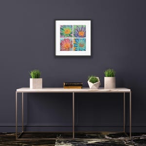 Puede incluir: Una obra de arte enmarcada con cuatro pinturas florales coloridas. Cada cuadrado muestra una flor diferente en tonos de verde, morado, rosa y azul, con centros naranjas. La obra cuelga sobre una mesa con tapa de mármol con plantas decorativas.