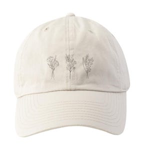 May include: A beige baseball cap with a simple line drawing of four different flowers on the front.