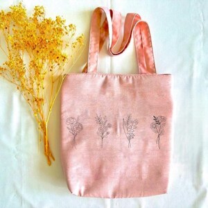 May include: A pink tote bag with a floral design. The bag has a single strap and is made of a soft, canvas-like material.