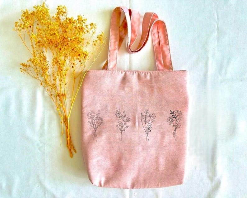 May include: A pink tote bag with a floral design. The bag has a single strap and is made of a soft, canvas-like material.