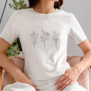 May include: A white t-shirt with a simple line drawing of three different bouquets of flowers on the front.