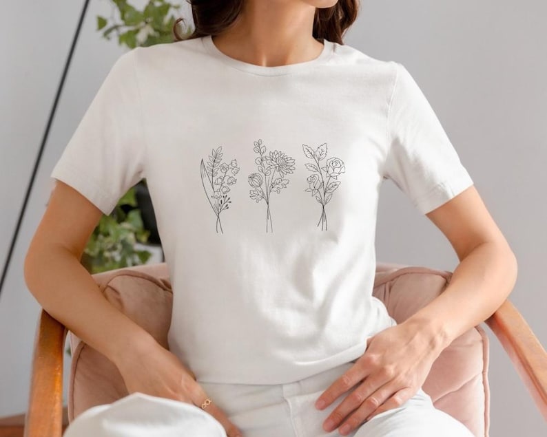 May include: A white t-shirt with a simple line drawing of three different bouquets of flowers on the front.