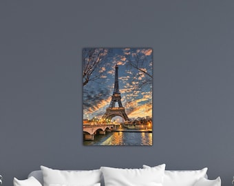 May include: A canvas print depicting the Eiffel Tower at dusk. The famous tower is set against a sky of orange, blue, and yellow hues. The Seine and a bridge are in the foreground, with lights reflecting on the water.