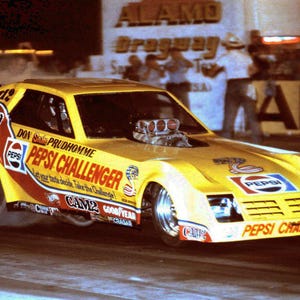 May include: A yellow and red drag racing car with the words "Don Prudhomme Pepsi Challenger" on the side. The car is in mid-air with the front wheels off the ground.