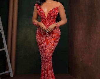 May include: A vibrant red, floor-length gown with a plunging neckline and detailed beadwork. The dress has long sleeves and a fitted bodice that flows into a flared skirt. The gown is a striking red, suitable for special occasions.
