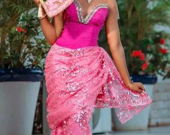 Peut inclure: Une femme porte un ensemble rose vif, comprenant un haut sans bretelles, une jupe en dentelle et un turban assorti. Elle tient un éventail rose avec des détails dorés. La tenue est ornée de motifs floraux et d'ornements complexes.