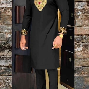 May include: Black tunic and pants set with gold embroidery. The tunic features ornate gold detailing around the neckline and cuffs, with a central heart-shaped design. The outfit is completed with black dress pants and shoes.